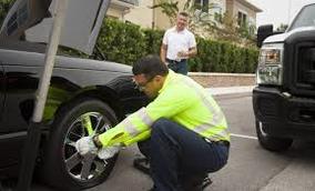 Man in yellow vest from roadside assistance changing a flat tire for a customer